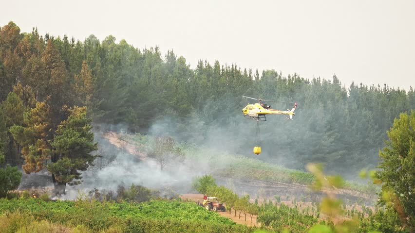 slow motion Aerial firefighting helicopter deploying bambi bucket, dropping water on raging forest fire, battling intense flames and preventing environmental destruction