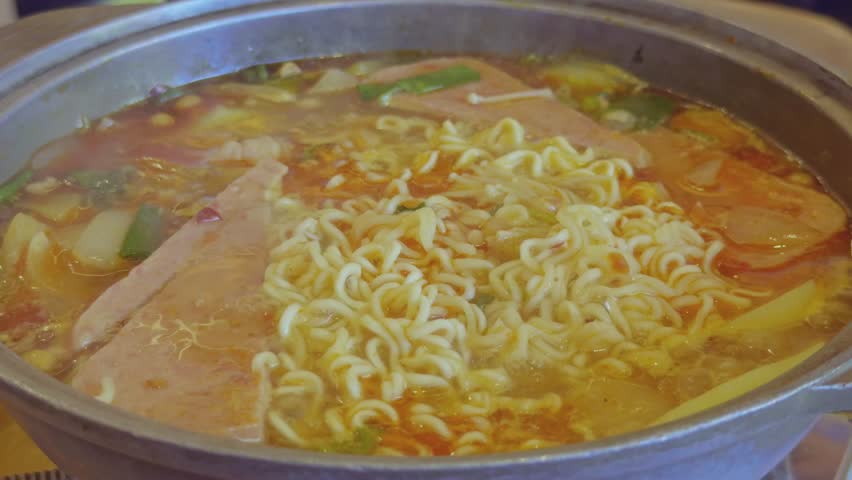 Close-up of a bubbling hot pot with instant noodles, vegetables, and meat slices cooking in broth. Perfect for Asian cuisine, comfort food, and dining themes.