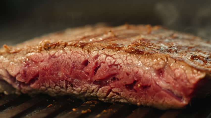 Cooking Beef angus steak in restaurant, close up Pieces of hot ribeye steak served on the wooden board. Medium steak slices with blood, salt and pepper in fancy meat cafe. 