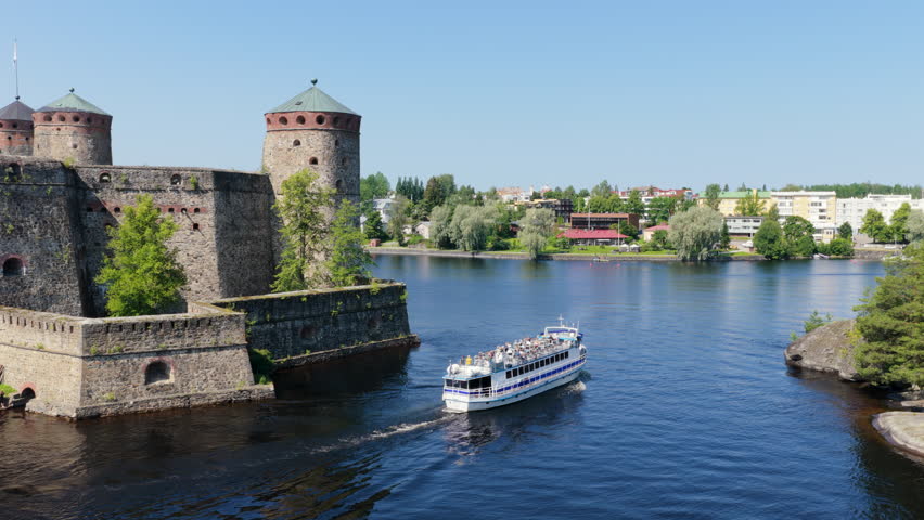 Aerial view of a tour boat passing the Olavinlinna castle, sunny day in Finland