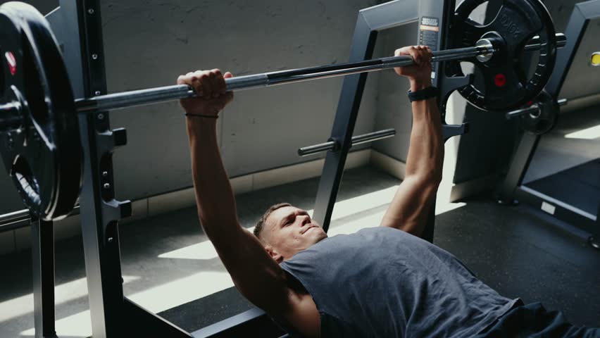 A man engaging in a bench press workout at the gym. He is lifting heavy weights for strength training, promoting fitness and muscle growth. Dedication and effort shown in his expression.