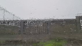 A gray day observed through a rain-streaked window. Raindrops heavily distort the view, creating abstract patterns on the glass. In the background, a weathered concrete wall is partially visible,  - Powered by Shutterstock - Get 15% off with code: PIKWIZARD15