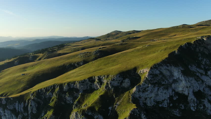 Hills covered in grass and rock formations Mountains in the distance under a clear sky Light and shadows on the landscape