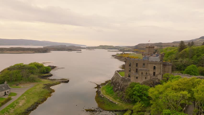Aerial drone shot of Dunvegan Castle on the Isle of Skye, Scotland, with a scenic bay in the background, surrounded by lush greenery and rugged coastal beauty.