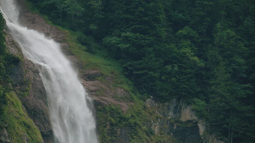 Tilt down shot of a waterfall going down rugged rock formations, sending mist and spray into the air, close up shot