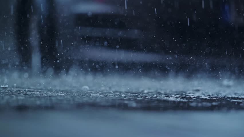 Slow motion rain droplets explode into puddles on asphalt parking surface
