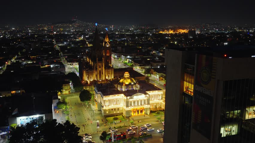 Traffic In Front Of MUSA Museum of the Arts Illuminated At Night With Parroquia El Expiatorio Eucarístico In The Background In Guadalajara, Jalisco, Mexico. - aerial shot