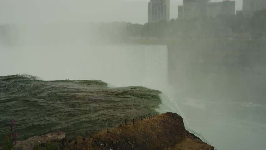 Mist rises from the roaring drop of Niagara Falls as rushing water surges over the rocky ledge into the gorge below.