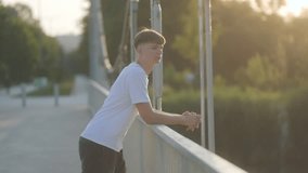 A lonely teenage boy leans over a bridge railing, lost in thought, as the golden light of sunset surrounds him. A peaceful yet emotional moment of self-reflection. - Powered by Shutterstock - Get 15% off with code: PIKWIZARD15