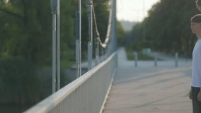 Wearing relaxed clothes, a teen boy leans over a railing on a quiet bridge, surrounded by greenery, in a mood of thoughtfulness and emotional solitude. - Powered by Shutterstock - Get 15% off with code: PIKWIZARD15