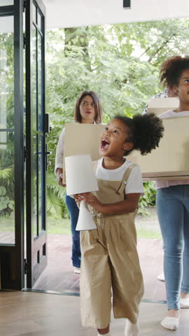 Vertical Screen : Happy African American young family bought new house. Mom, Dad, and child smiling happy hold cardboard boxes for move object walking into big modern home. New real estate dwelling.