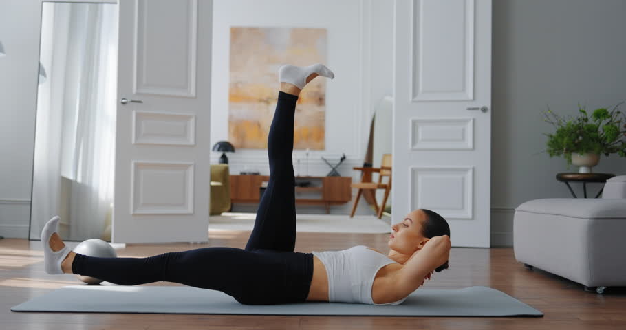 Athletic woman performing core workout on yoga mat in modern living room with natural light