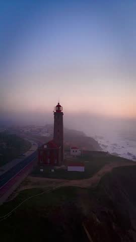 An orbiting vertical, aerial footage of Penedo da Saudade Lighthouse (Farol Penedo da Saudade) against dusk sky at sunset in Marinha Grande, Portugal
