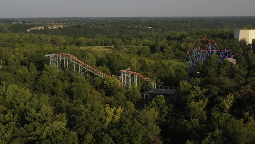 Aerial view of roller coasters weaving through lush green trees, contrasting with the bright colors of the amusement park rides, Mason, Ohio, United States.