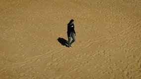 Woman walking barefoot over empty sandy terrain with scattered footprints. Female moving across sunlit beach surface in solitude. Lady strolling calmly through golden sand leaving light trail - Powered by Shutterstock - Get 15% off with code: PIKWIZARD15