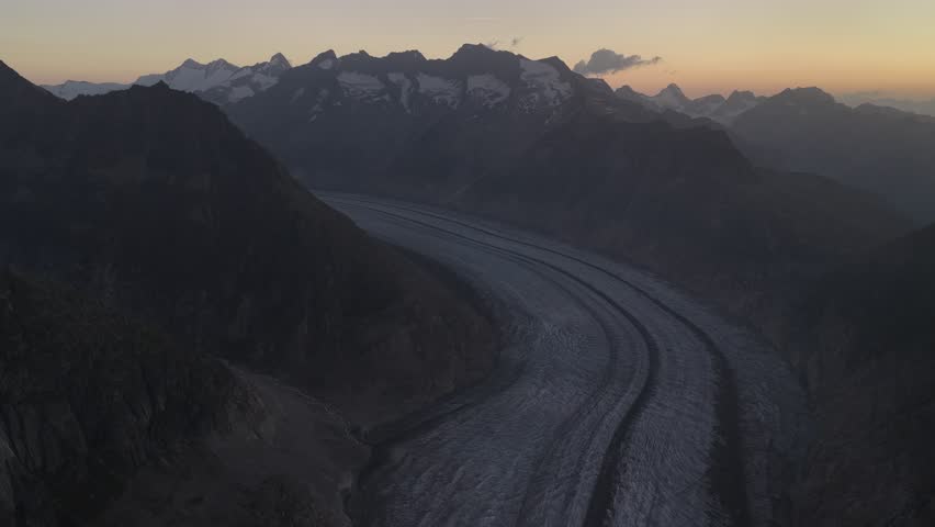 Aerial view of the majestic Aletsch Glacier snaking through rugged mountains, the landscape bathed in the soft glow of twilight, Fieschertal, Valais, Switzerland.