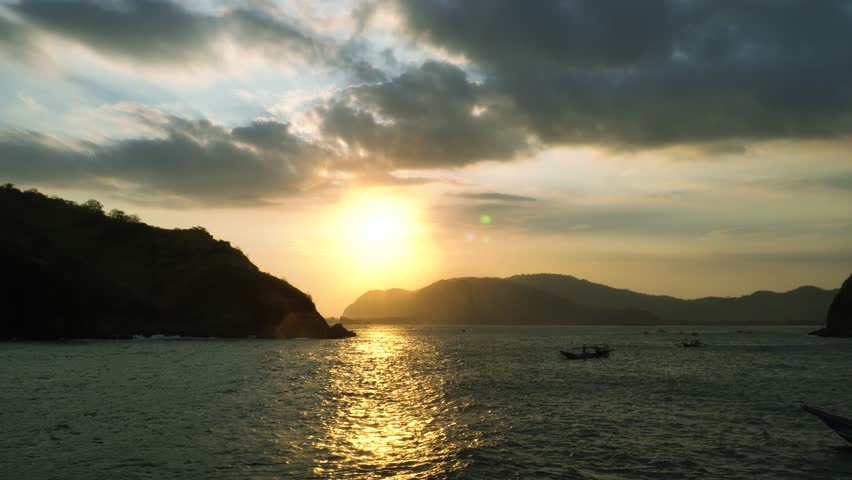 Sunset over ocean waves wash sand beach. Aerial sun set above mountain silhouette.