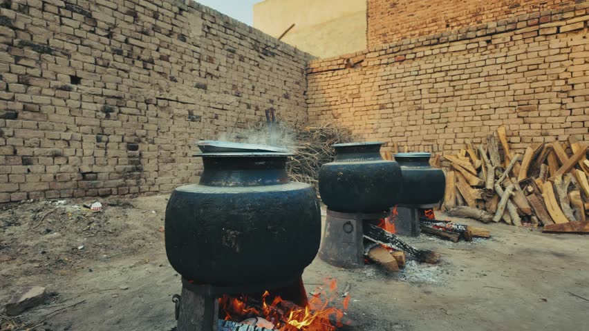 Three large traditional daigs (cooking pots) placed on open wood fires inside a brick-walled courtyard in Chichawatni, Pakistan