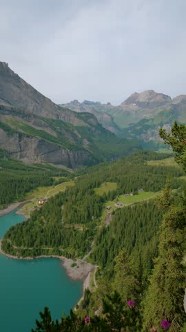 Turquoise alpine lake surrounded by lush green forests and dramatic rocky cliffs in the Swiss Alps, pan shot