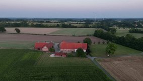 Traditional German farmhouse with red roofs, surrounded by fields, trees and wind turbines in rural countryside at sunset. Aerial orbiting shot. Dusk scene in Germany. Large property area in suburb. - Powered by Shutterstock - Get 15% off with code: PIKWIZARD15
