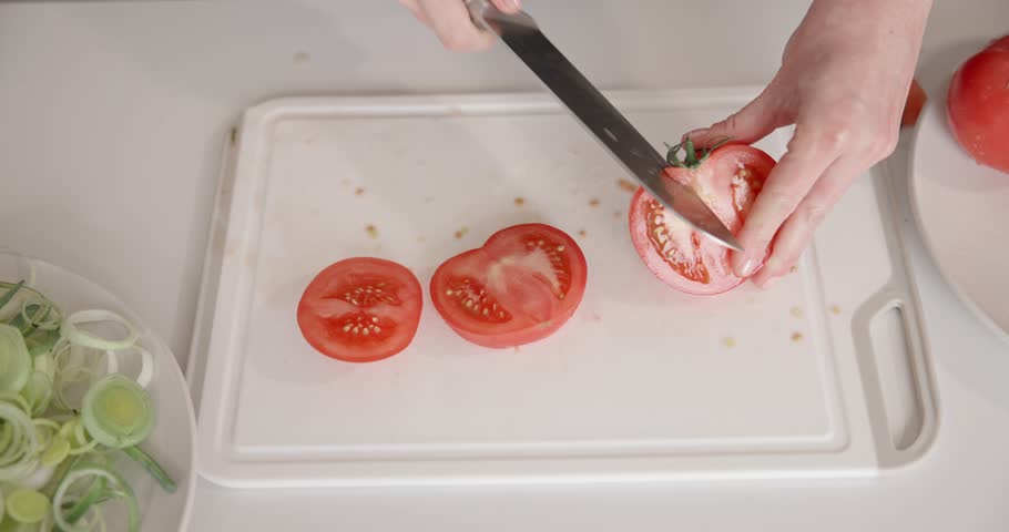 Cooking at home - woman in small apartment cutting santoku on vegetable cutting board fresh organic tomatoes. High quality 4k footage