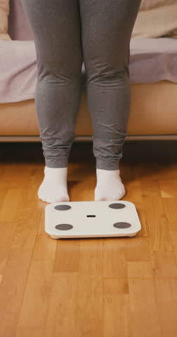 Female legs step onto white electronic scales. Adult woman positions feet firmly on surface to check current body weight during home monitoring