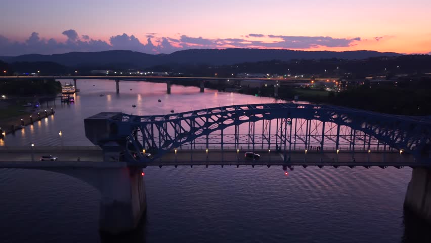 Dramatic colorful sunset sky over the John Ross Bridge in Chattanooga, aerial following cars over Tennessee River with tranquil twilight evening