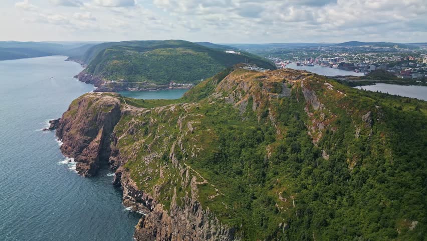 A drone soars above the craggy cliffs of Signal Hill, revealing a green headland with steep drops into the Atlantic and glimpses of St. John’s harbour in the distance.