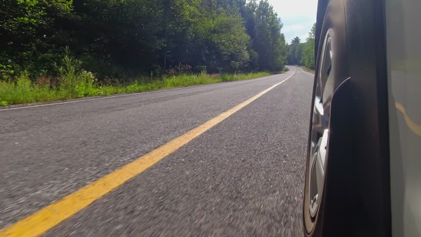 Cinematic POV of front left car wheel driving plate. Driving on asphalt in rural area with vegetations. Background for LED volumes. Immersive realistic driving footage for film virtual production.