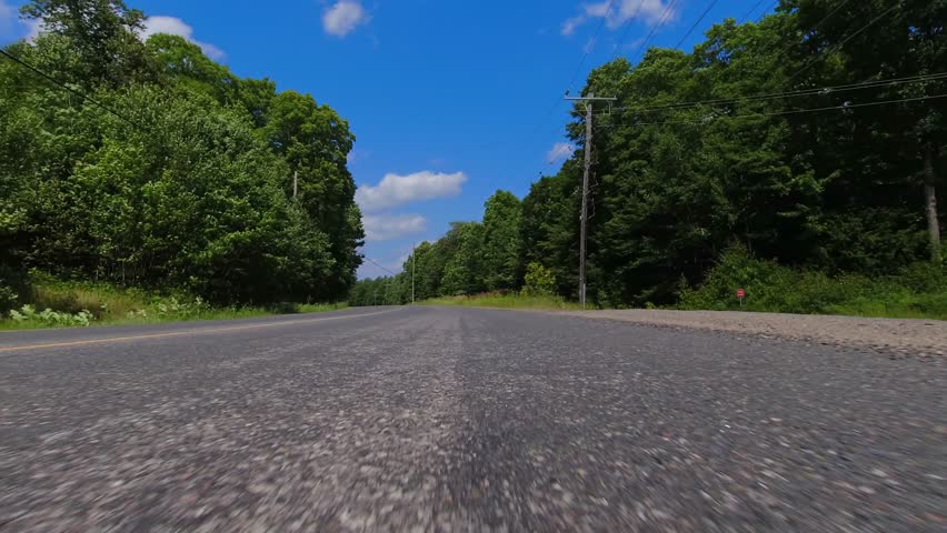 Cinematic car driving plate POV front bottom bumper view, immersive realistic driving footage for film and television virtual production. Driving on asphalt in rural area. Background for LED volumes.