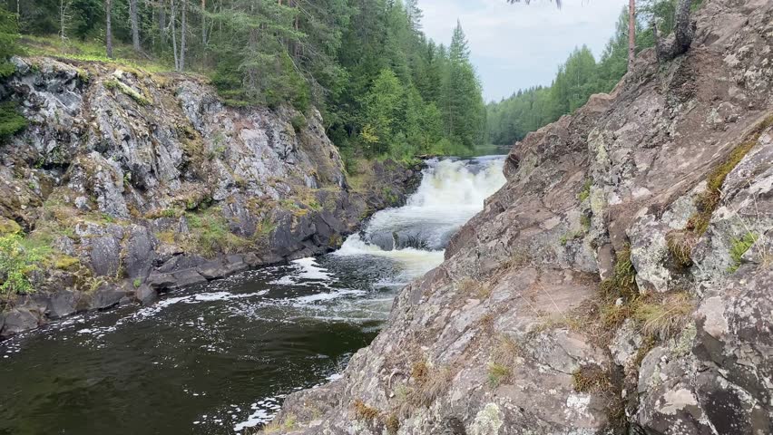 Beautiful landscape with waterfall in northern forest on summer evening. Powerful stream of water among stone rocks and green foliage. Kivach waterfall at Suna river in Karelia, Russia. With sound