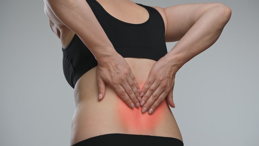 A woman rubs her lower back highlighted by a red halo, indicating pain or injury. Low back pain can be caused by a variety of factors. The concept of health, treatment and pain relief.
