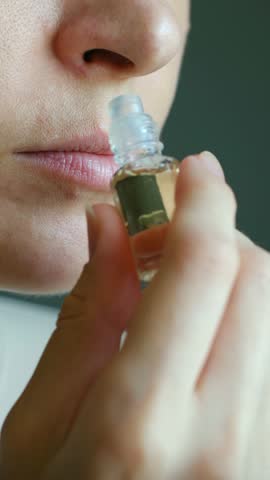 Elegant female hand delicately holding transparent perfume bottle, deeply inhaling luxurious fragrance with closed eyes and sensory appreciation. Woman smelling perfume from small bottle. 