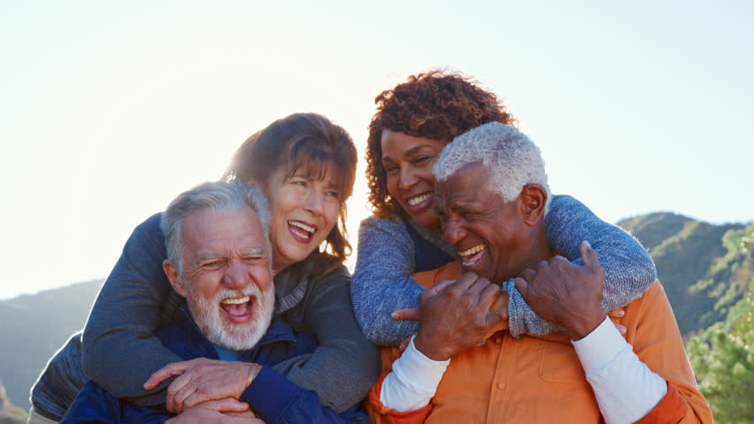 Portrait Of Group Of Senior Friends On Hike In Countryside Laughing Into Camera With Lens Flare