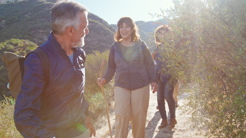 Group Of Senior Friends Go Hiking Along Trail In Countryside Together