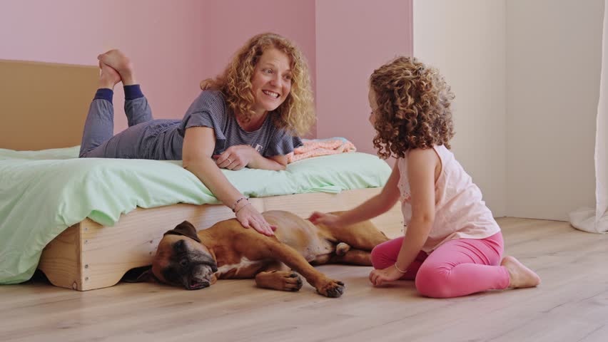 Mother and daughter petting boxer dog in bedroom