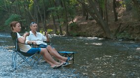 Couple enjoying coffee by the river in camping chairs. Peaceful riverside morning with tourists drinking coffee, resting in chairs and immersing themselves in serene natural surroundings - Powered by Shutterstock - Get 15% off with code: PIKWIZARD15