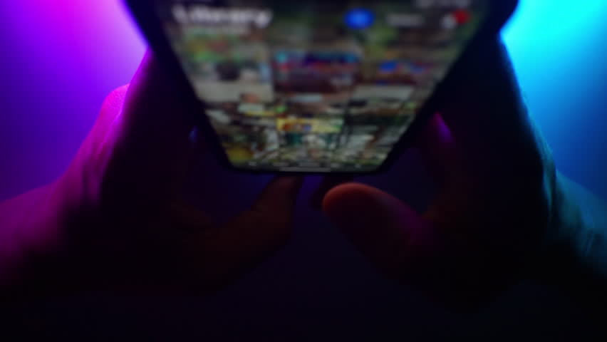 Close up of fingers touching and scrolling on mobile application. On a blue and purple neon tones background. Internet browsing, Social media marketing. Blurred macro. Top view dark shot