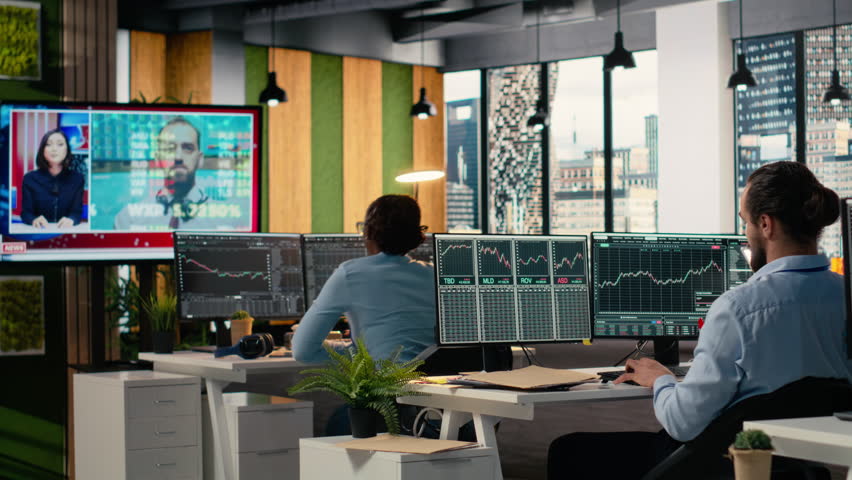 Traders in office follow TV coverage of Black Swan event shaking global finance, calling clients to withdraw money. Anxious investors seeing portfolio value loss caused by bear market crisis, camera B