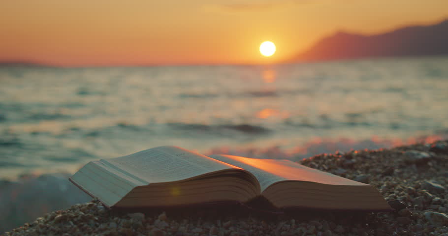 Open book lying on a pebbled beach with sunset over the sea in summer Croatia