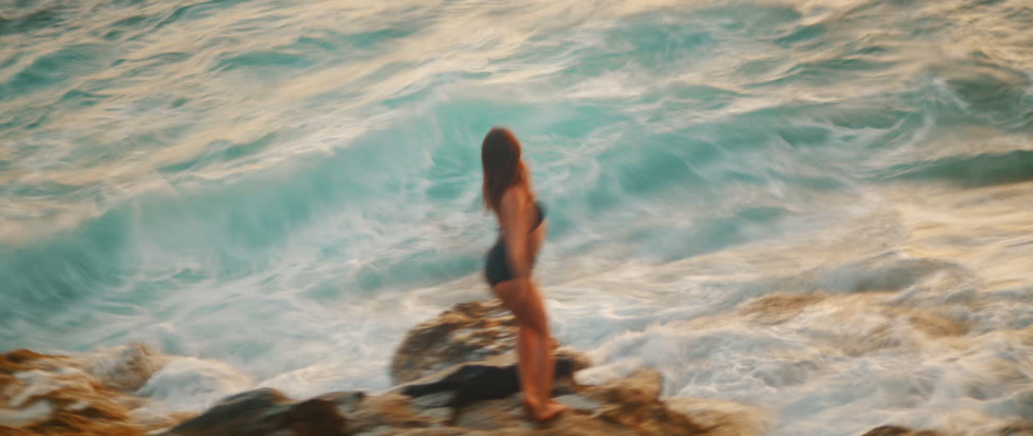 Female dancer raises arm near ocean with expressive body motion