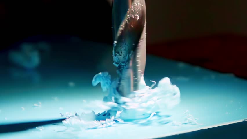 An extreme close-up, slow-motion shot shows a metal drill bit boring a hole into a sheet of blue plastic, sending beautiful curly shavings spiraling upwards from the surface.