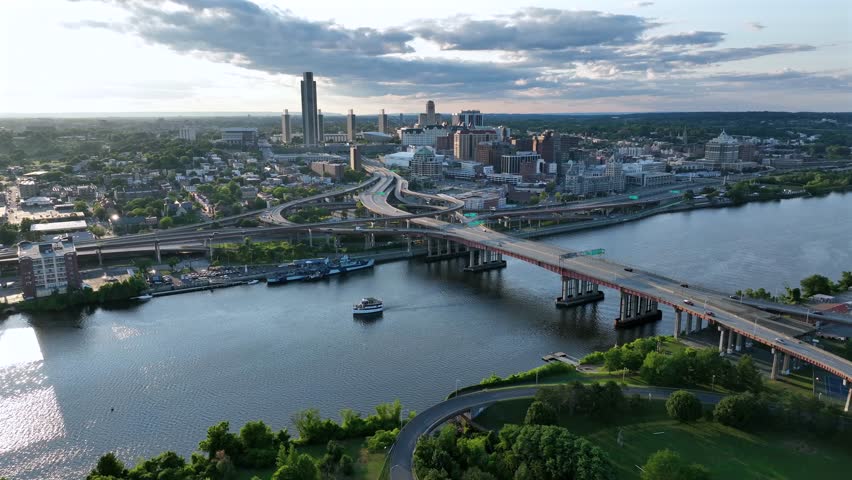 Cars on Dunn Memorial Bridge crossing Hudson River in Albany, New York. Sunset time in summer. Aerial wide shot. Albany city skyline in downtown. Multi level elevated highway leading to city.