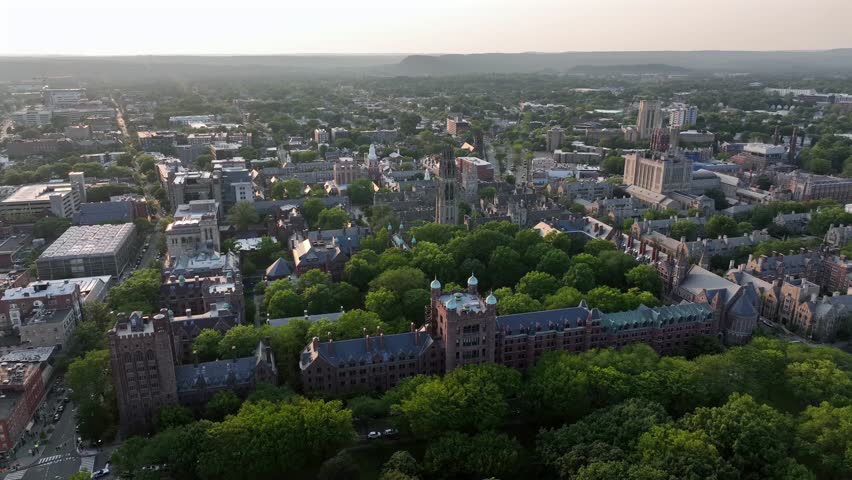 Yale university in gothic style during golden sunset in New Haven, Connecticut. Aerial wide shot. Green trees inside inner yard of campus.