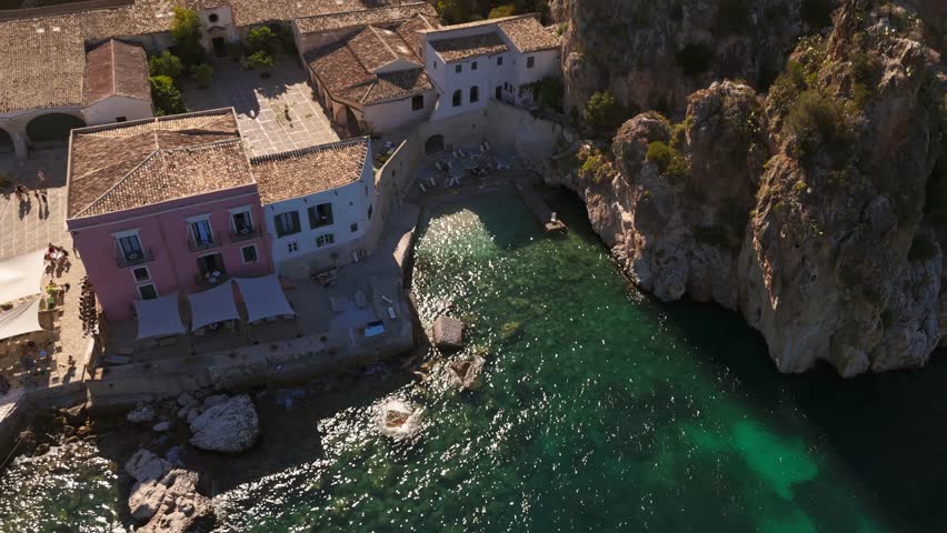 Aerial drone flying over Tonnara di Scopello, Sicily, Italy, showcasing its rocky coastline, turquoise waters, and historic tuna fishery during Italian summer, with scenic views of cliffs