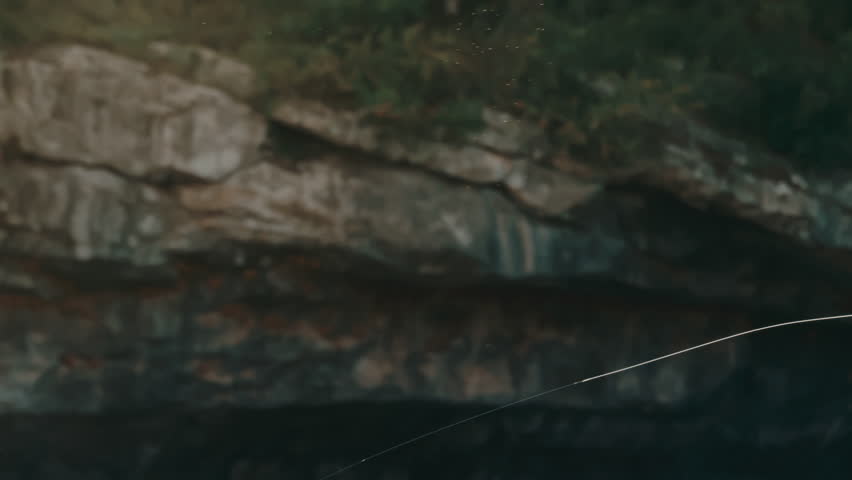 Golden hour slow motion follow shot of fly fishing line arcing gracefully through the air above shimmering river