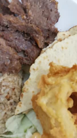 A close-up video shows a delicious plate of doner kebab with deliciously seasoned meat slices, fluffy rice, crispy fried onion rings, and a refreshing salad.