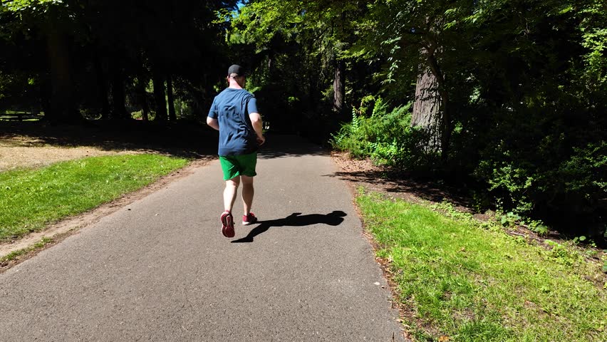 A jogging man in Laurelhurst Park in Portland Oregon, USA, with trees, paths, and summer greenery, captured on a pocket camera with gimbal stabilizer for 4K smooth motion footage.