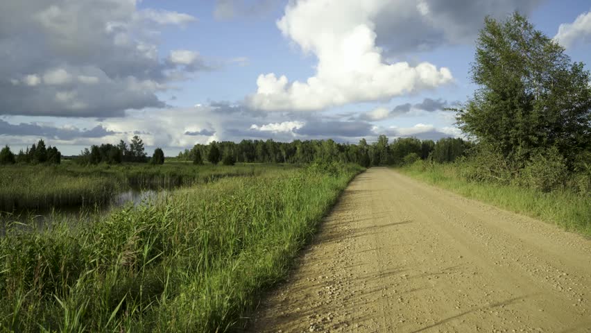Landscape of the road in the evening along the lake shore in summer. The dirt road with crushed stone goes into perspective. Beautiful clouds over the water. Lake Kanieras in Latvia