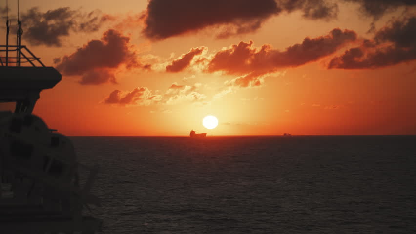 Silhouette of Cargo Ship Sailing Across Ocean at Golden Sunset with Dramatic Clouds